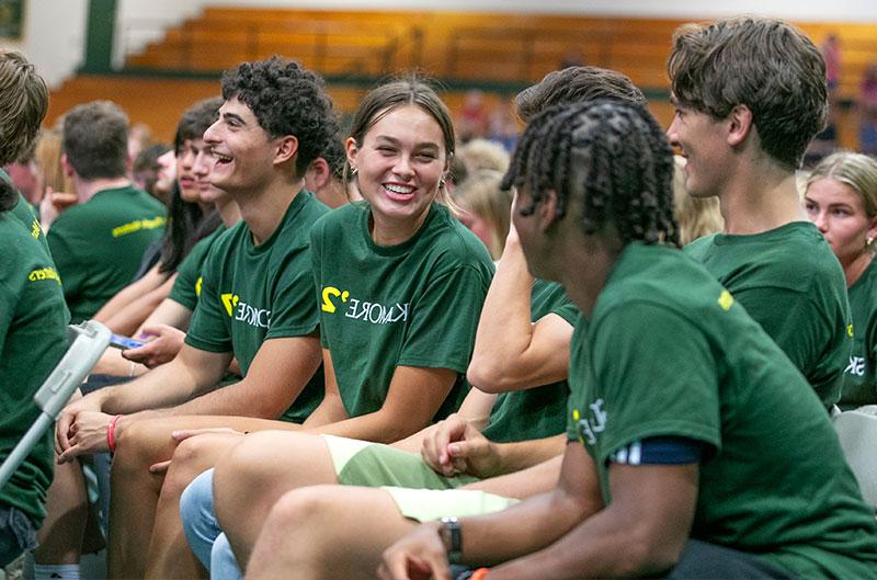 学生们穿着印有“365买球官网”字样的绿色衬衫，坐在体育馆里互相问候